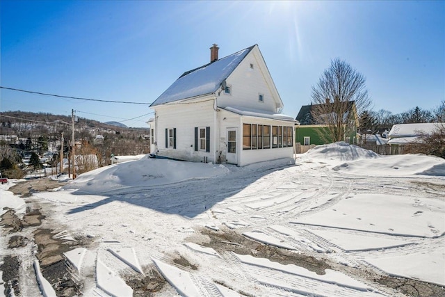 snow covered rear of property featuring a sunroom and a chimney