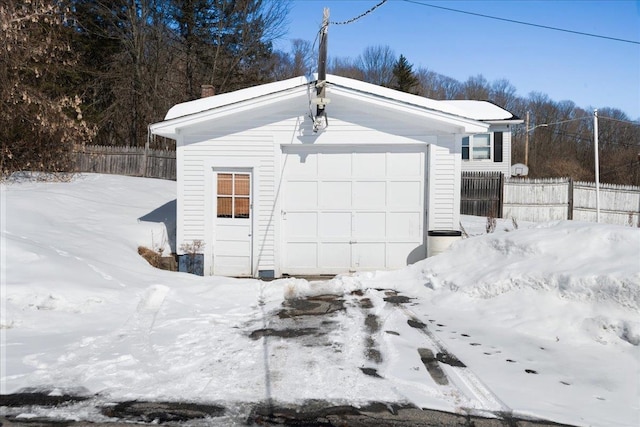 snow covered garage with fence and a detached garage