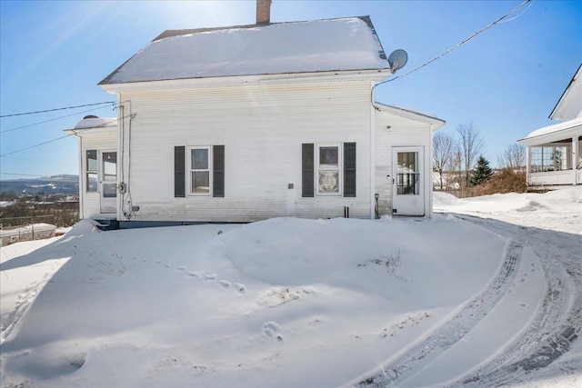 snow covered rear of property with a chimney