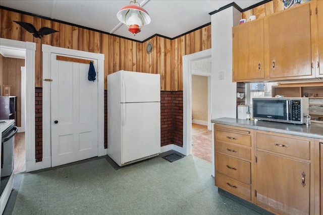 kitchen with wood walls, stainless steel microwave, freestanding refrigerator, and tile patterned floors