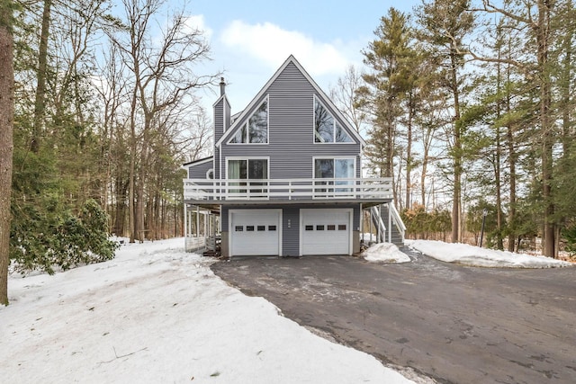 view of snow covered exterior with a chimney, aphalt driveway, an attached garage, stairs, and a wooden deck