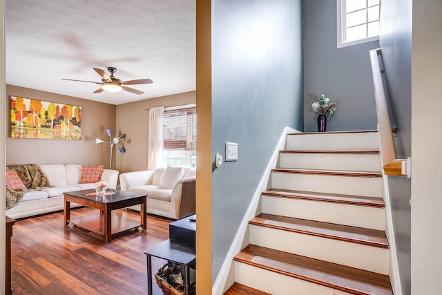 staircase with a ceiling fan, a textured ceiling, and wood finished floors