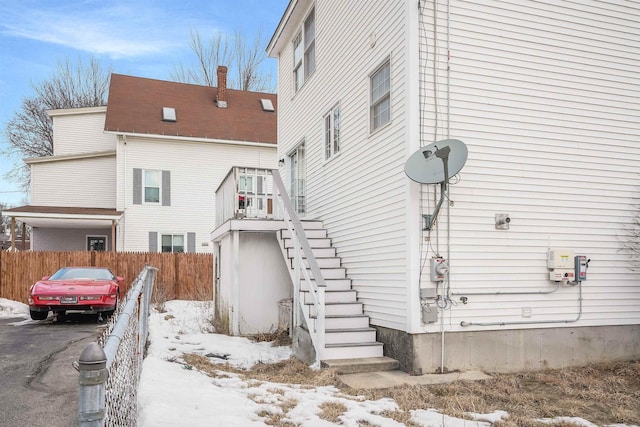 view of snowy exterior featuring a chimney, fence, and stairway