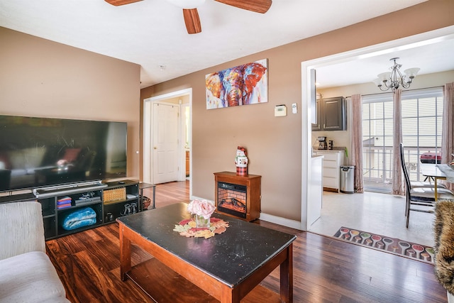 living area with ceiling fan with notable chandelier, baseboards, and wood finished floors