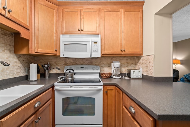 kitchen with white appliances, backsplash, dark countertops, and a sink