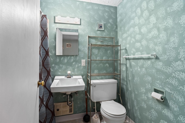 bathroom with toilet, wallpapered walls, baseboards, and a sink