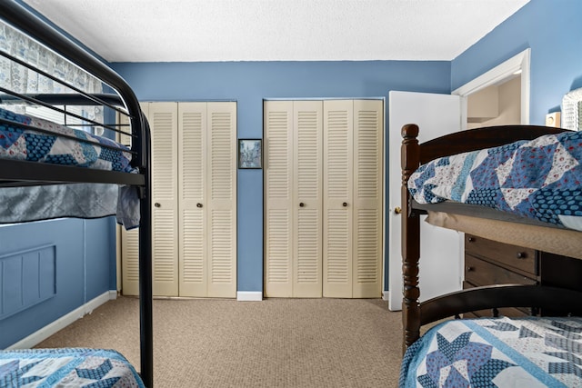 carpeted bedroom featuring a textured ceiling, two closets, and baseboards