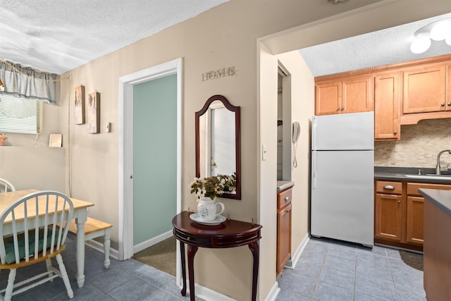 kitchen with a textured ceiling, light tile patterned flooring, backsplash, and freestanding refrigerator