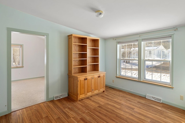 unfurnished room with light wood-style floors, baseboards, visible vents, and vaulted ceiling