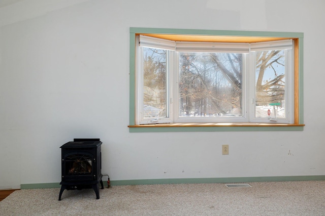 details with a wood stove, baseboards, visible vents, and carpet flooring