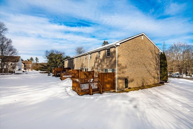 snow covered property with brick siding and a deck