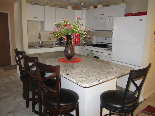 kitchen with white appliances, white cabinets, a kitchen island, a breakfast bar area, and a sink