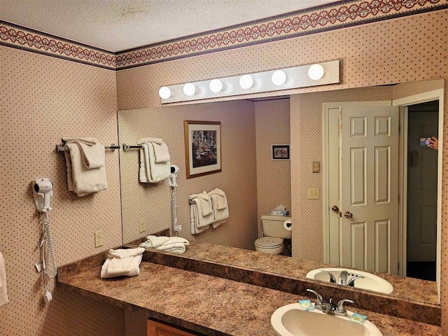 bathroom featuring vanity, a textured ceiling, toilet, and wallpapered walls