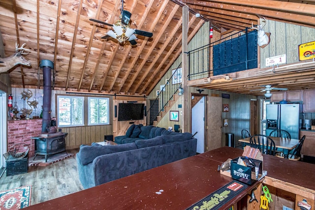 living area featuring a wood stove, high vaulted ceiling, wood finished floors, ceiling fan, and stairs