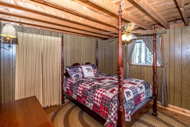 bedroom with wooden walls, beamed ceiling, ceiling fan, and wood finished floors