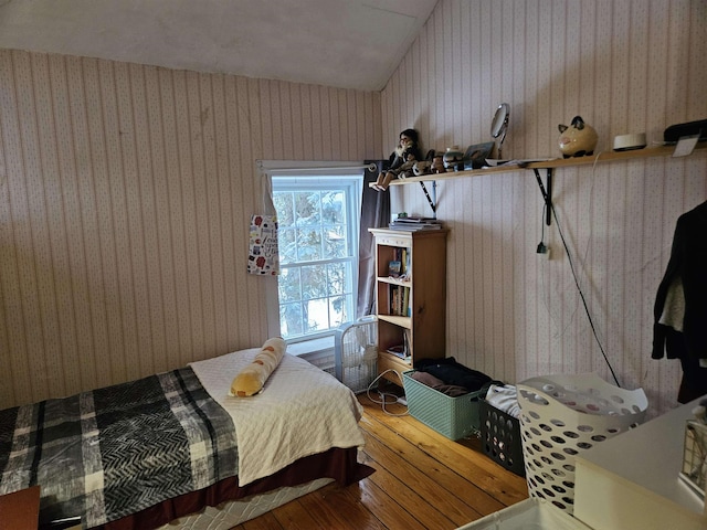 bedroom with lofted ceiling, wood finished floors, and wallpapered walls