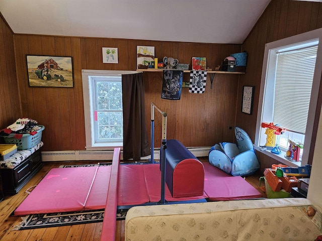 playroom with lofted ceiling, a baseboard heating unit, wood walls, and wood finished floors