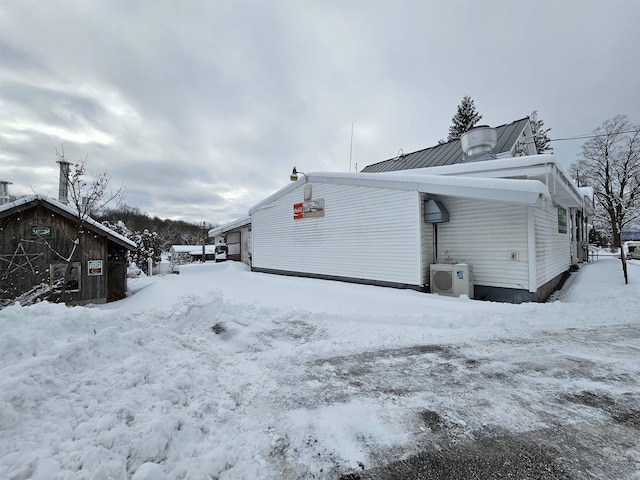 snow covered property with a garage, a standing seam roof, metal roof, and ac unit