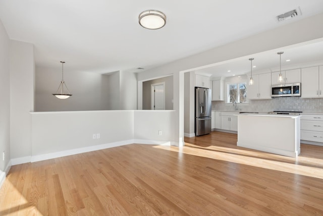 kitchen featuring stainless steel appliances, tasteful backsplash, visible vents, light wood-style flooring, and a sink