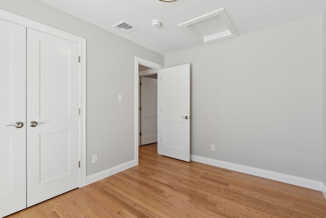 unfurnished bedroom with visible vents, light wood-type flooring, attic access, and baseboards