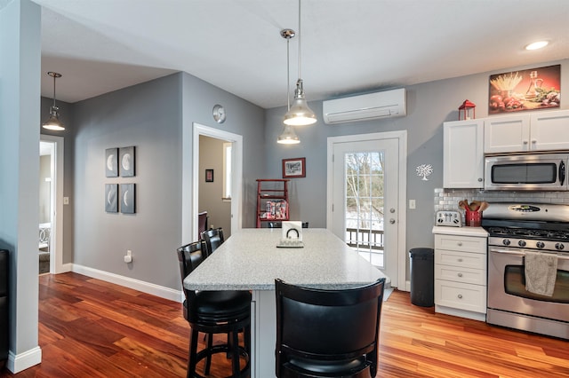 kitchen with a wall unit AC, stainless steel appliances, backsplash, white cabinets, and wood finished floors