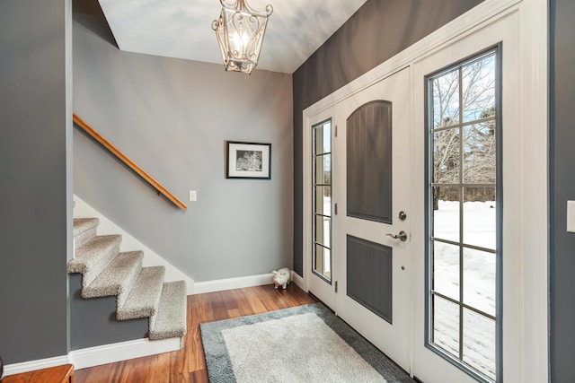 foyer entrance with stairs, a chandelier, baseboards, and wood finished floors