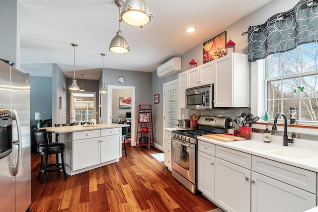 kitchen with wood finished floors, a wall mounted air conditioner, a sink, stainless steel appliances, and backsplash