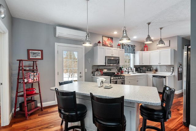 kitchen with tasteful backsplash, appliances with stainless steel finishes, a sink, a wall mounted air conditioner, and a kitchen breakfast bar