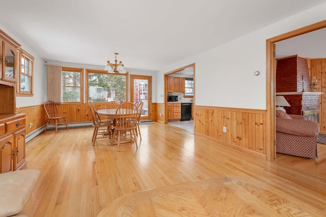 dining room with light wood-type flooring, wood walls, a baseboard radiator, and wainscoting