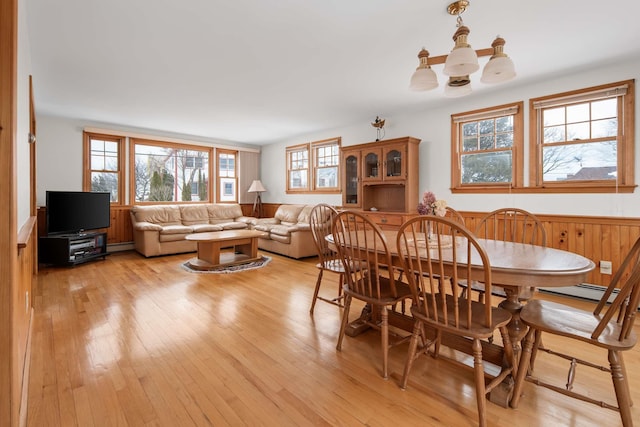 dining space featuring a notable chandelier, a baseboard heating unit, wainscoting, and light wood-style floors