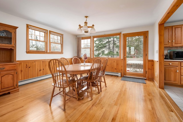 dining room featuring light wood finished floors, baseboard heating, a notable chandelier, and wainscoting