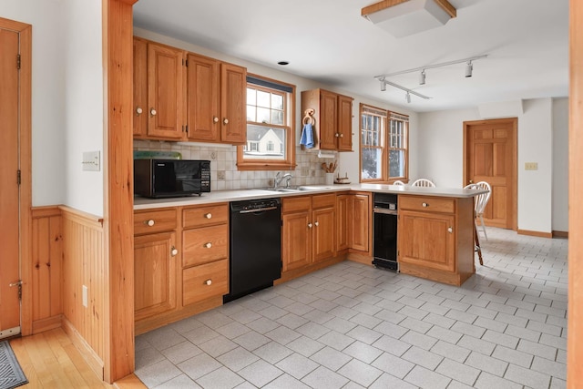 kitchen with wainscoting, a peninsula, light countertops, black appliances, and a sink