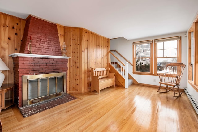 living area featuring wood-type flooring, baseboard heating, a brick fireplace, wood walls, and stairs