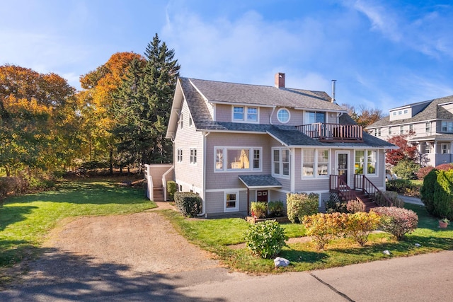 shingle-style home with a front lawn, a chimney, a shingled roof, and a balcony