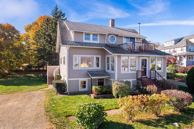 shingle-style home featuring a chimney, roof with shingles, a balcony, and a front lawn