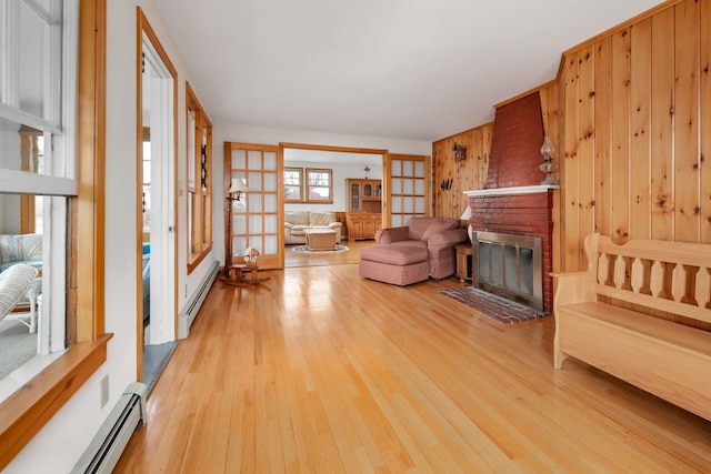 unfurnished living room featuring a baseboard heating unit, a fireplace, wood walls, and light wood finished floors