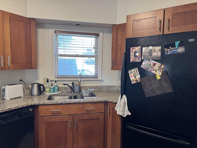 kitchen with brown cabinetry, a sink, light stone counters, and black appliances