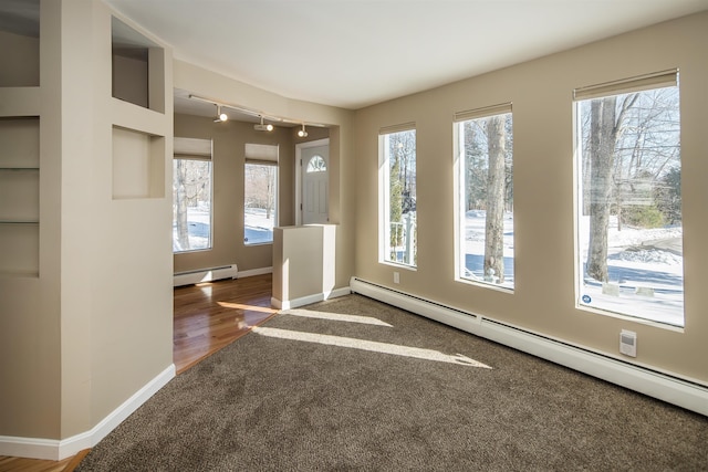 interior space with a baseboard heating unit, a wealth of natural light, and baseboards