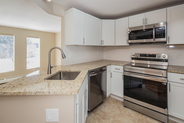 kitchen featuring decorative backsplash, appliances with stainless steel finishes, a peninsula, light stone countertops, and a sink