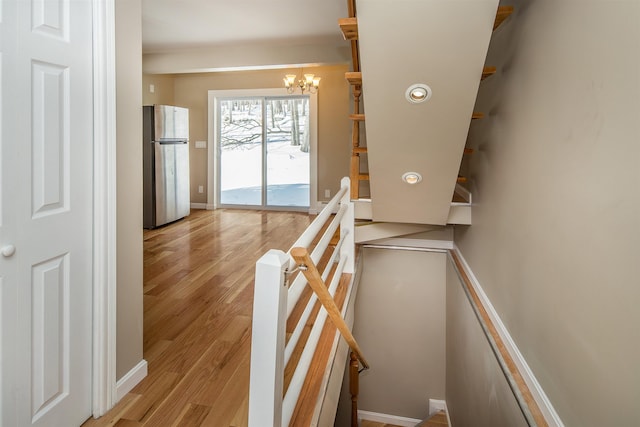 stairs featuring baseboards, wood finished floors, and an inviting chandelier