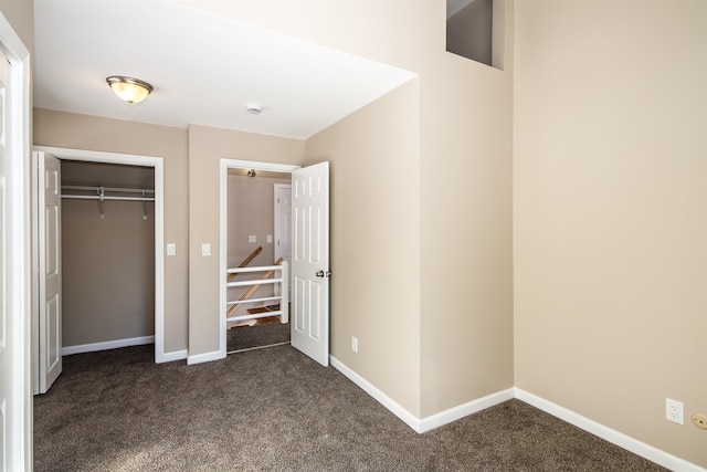 unfurnished bedroom with a closet, dark carpet, and baseboards