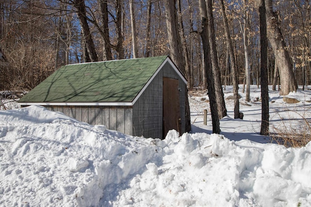 snow covered structure with a forest view and an outdoor structure