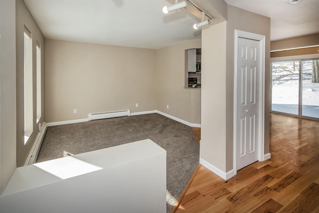 spare room featuring a baseboard radiator, rail lighting, baseboards, and wood finished floors