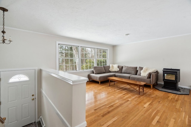 living area featuring a baseboard radiator, light wood-style floors, ornamental molding, a wood stove, and an inviting chandelier