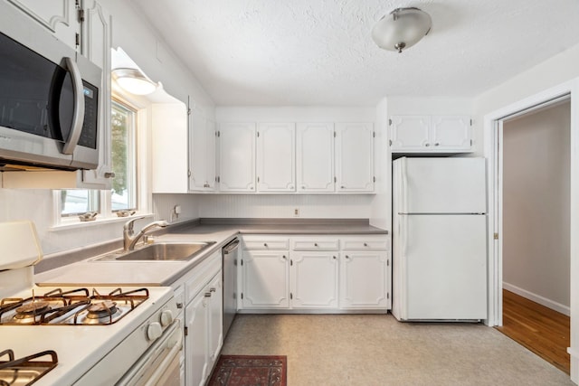 kitchen featuring a textured ceiling, stainless steel appliances, a sink, white cabinetry, and light floors