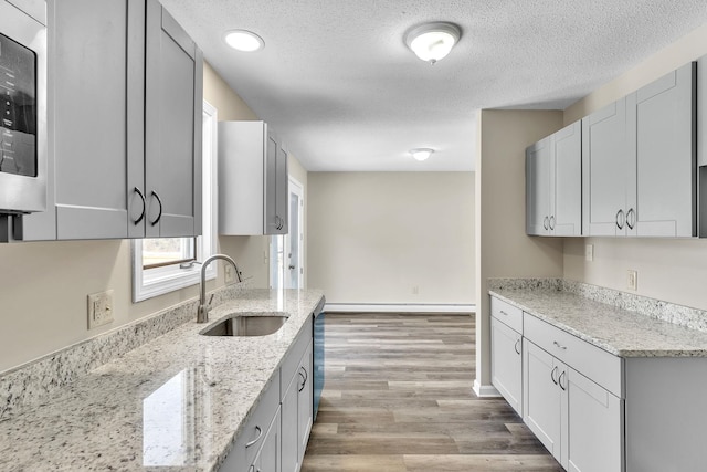 kitchen with light wood finished floors, baseboard heating, appliances with stainless steel finishes, a sink, and light stone countertops