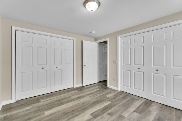 unfurnished bedroom with multiple closets, light wood-style flooring, and baseboards