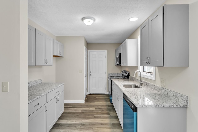 kitchen with light stone counters, wood finished floors, stainless steel appliances, a textured ceiling, and a sink