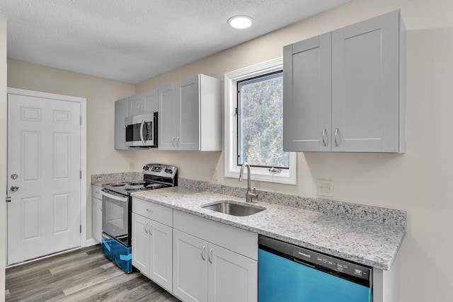 kitchen with appliances with stainless steel finishes, a sink, light stone counters, and light wood-style floors