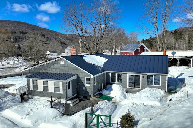 snow covered property with entry steps, metal roof, a standing seam roof, and a fenced front yard